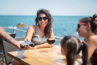 Eine junge Frau bezahlt im Ausland am Meer mit der Debit- oder Kreditkarte.